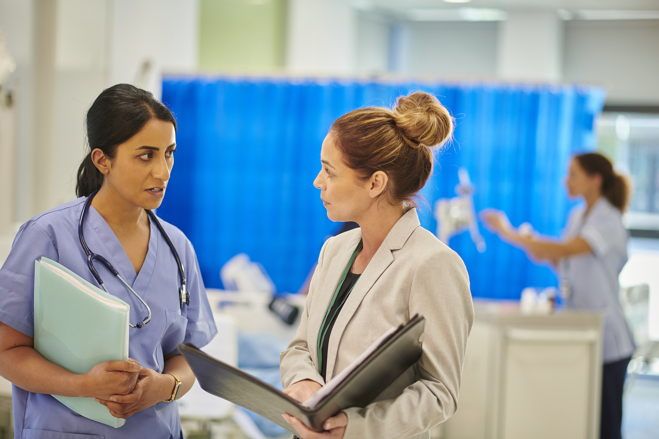 A health administrator talks with a nurse in a hospital corridor.