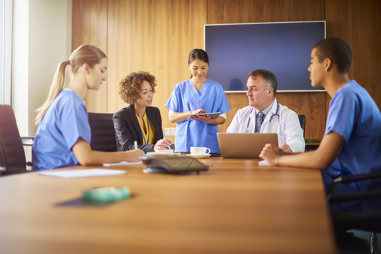 A team of nurses sitting with a doctor and a lawyer in a conference room.