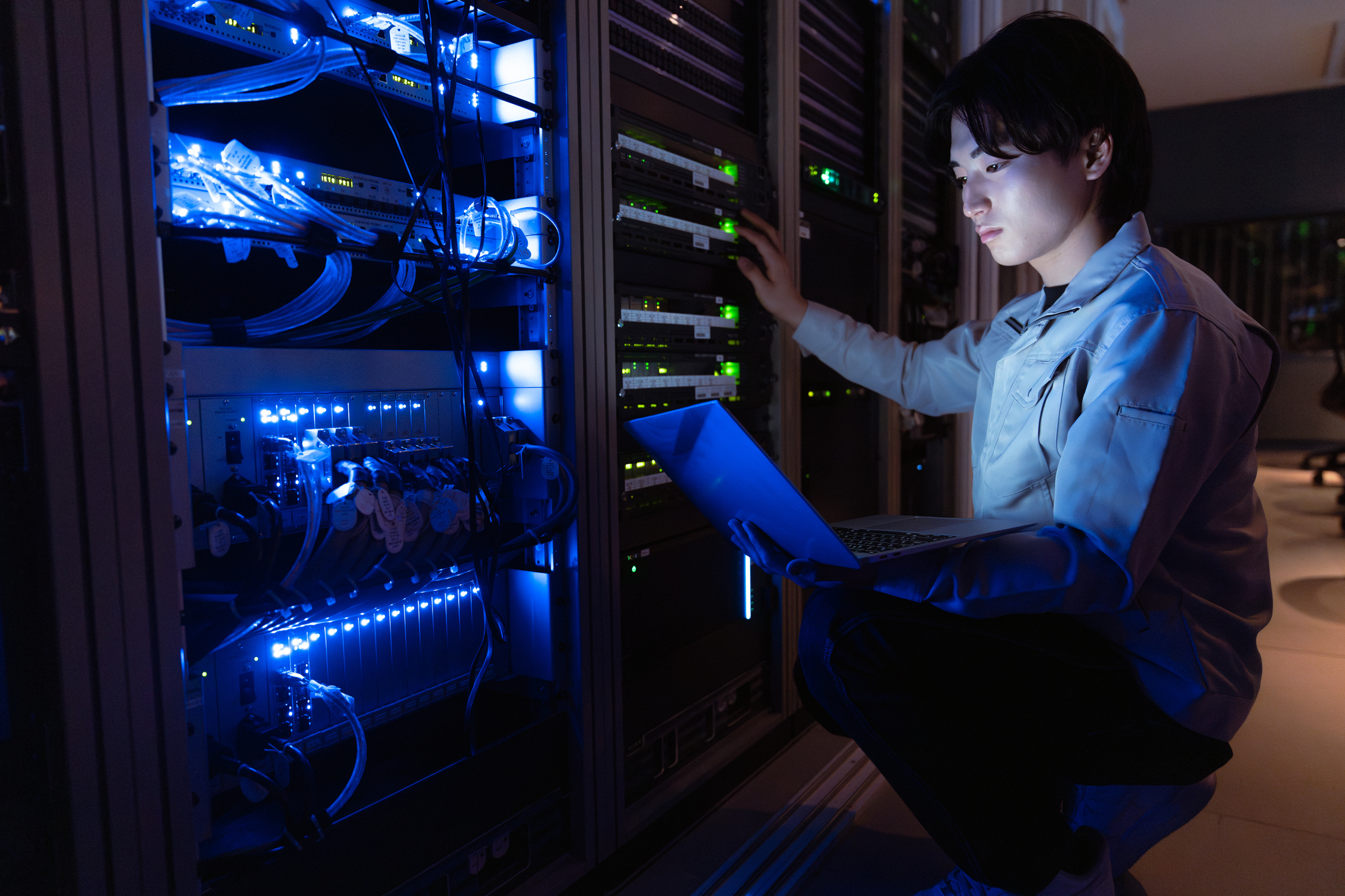 An IT professional consults a laptop while working on a server array.